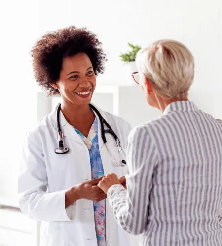 Smiling female doctor holding hands with older female patient in medical office during consultation