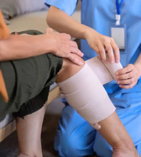 Medical professional wrapping a compression bandage around a patient's injured knee indoors