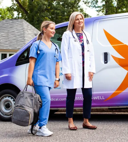 Two healthcare professionals standing next to a purple and white medical transport van outside a residential area.