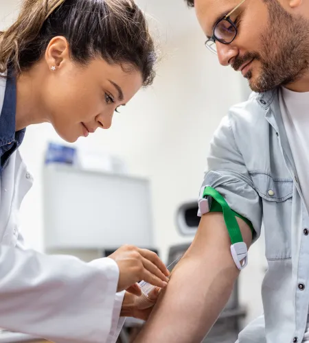 Doctor preparing to draw blood from a male patient's arm using a tourniquet and needle in a clinical setting