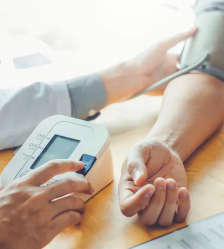 Person measuring blood pressure using digital monitor on arm in a medical setting.