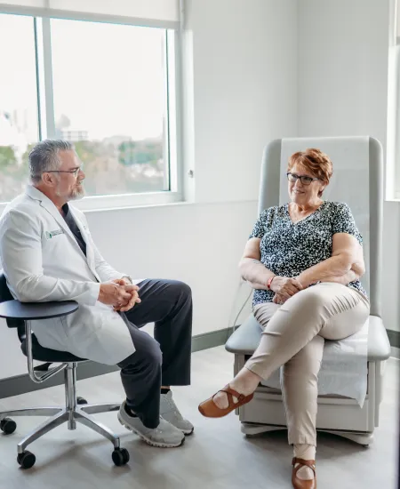 Doctor in white coat consulting with female patient in bright medical office with large windows.
