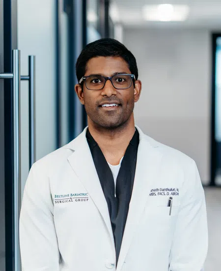 Smiling male doctor wearing glasses and white coat standing in a modern medical hallway