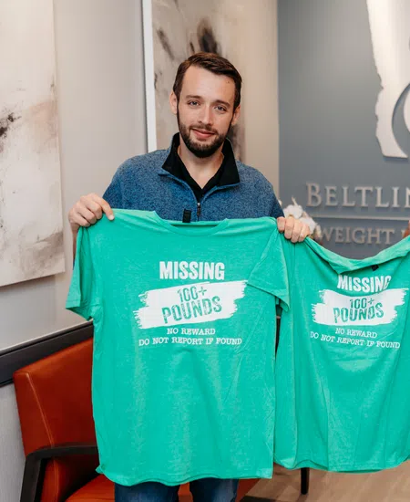 Two men holding green T-shirts with text Missing 100+ pounds promoting weight loss success at a clinic.
