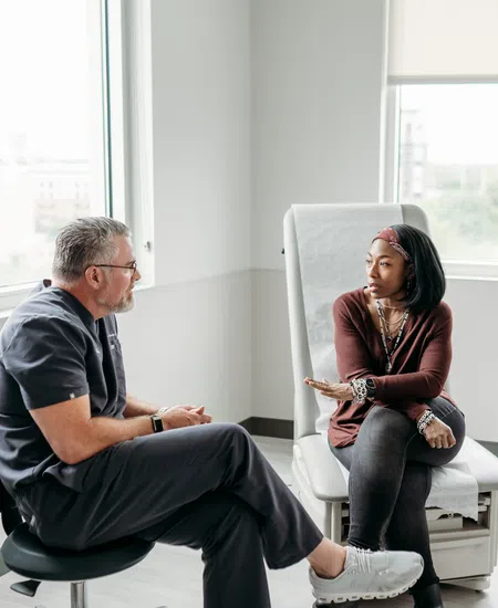 Female patient discussing health concerns with doctor in bright medical office with large windows.
