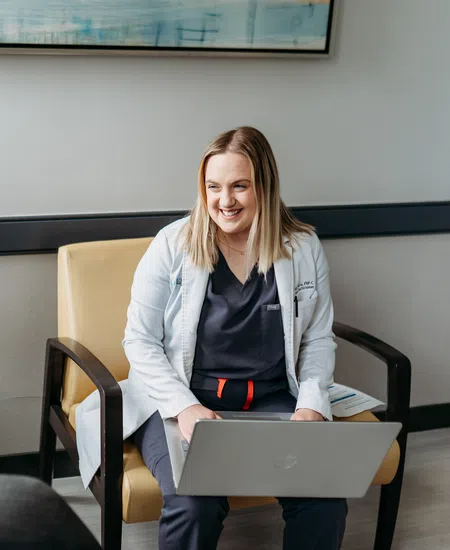 Female doctor with laptop smiling and consulting a patient in a modern medical office with orchid plant.