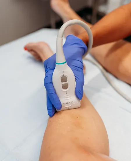 Medical professional using ultrasound device on patient's leg during a diagnostic examination.