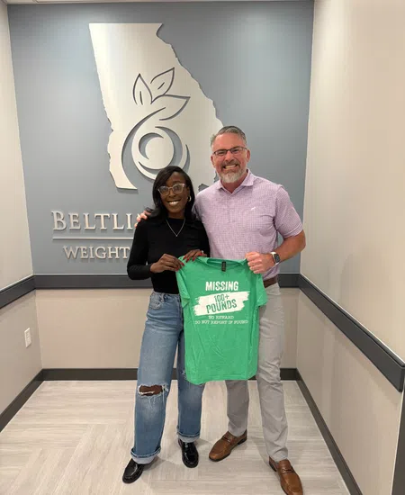 Man and woman smiling while holding a green weight loss t-shirt in an office lobby