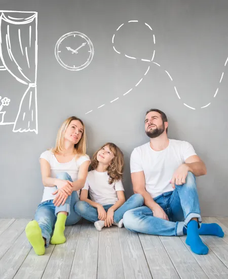 a woman and two girls sitting on a wood floor in front of a wall with drawings