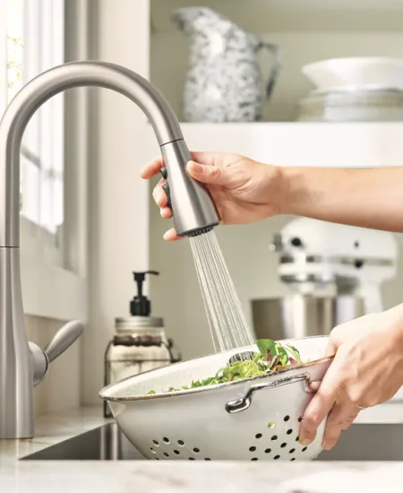 a person washing vegetables with kitchen sink faucet