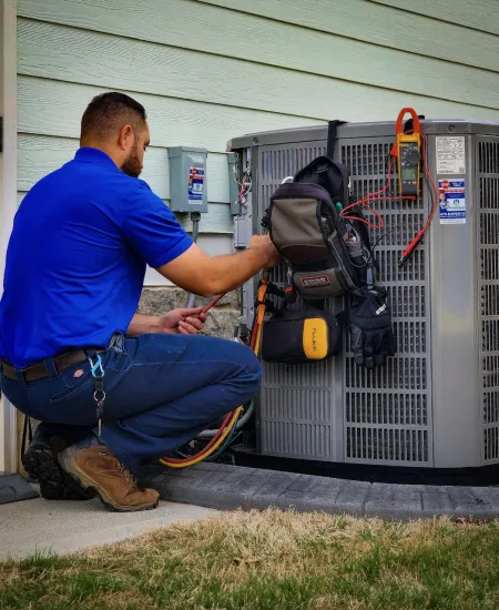 Technician in blue shirt repairing a residential HVAC unit with tools and diagnostic equipment outdoors.