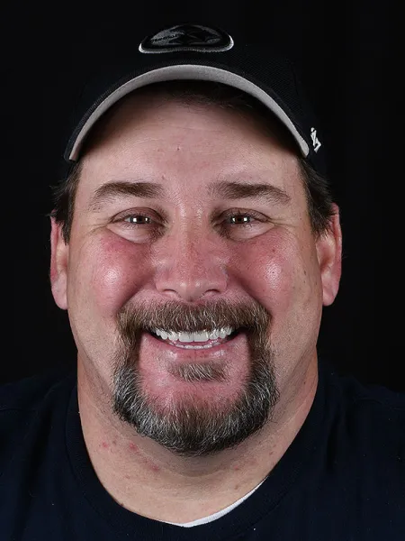 Smiling man in a baseball cap against a dark background, showcasing a friendly expression.