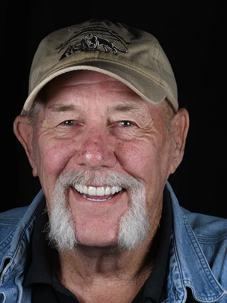 Smiling elderly man with a hat and denim jacket, showcasing a warm and friendly expression.