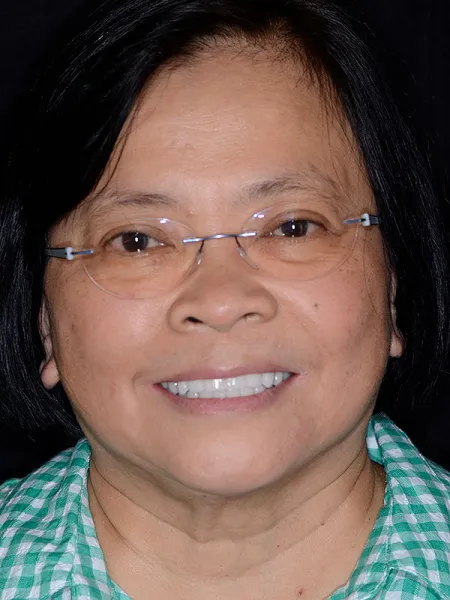 Smiling woman with glasses, wearing a checkered shirt, against a black background.