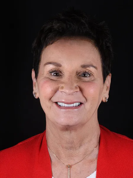 Smiling woman with short dark hair wearing a red blazer against a black background.