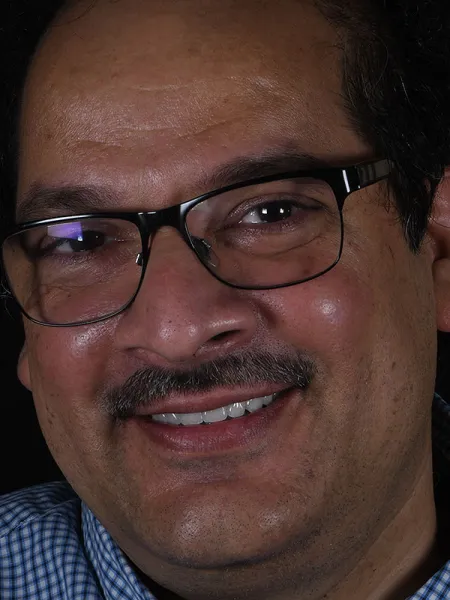Close-up portrait of a smiling man with glasses against a dark background.
