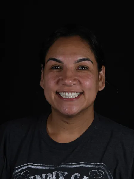 Smiling woman with dark hair wearing a black Johnny Cash printed t-shirt on a black background.