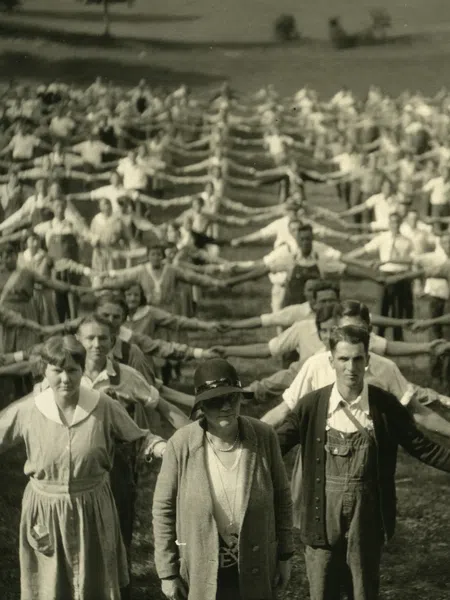 Large group of people standing outside holding hands in a long, interconnected line across a grassy field.