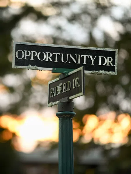 Street signs for Opportunity Drive and Fairfield Drive against a blurred sunset background.