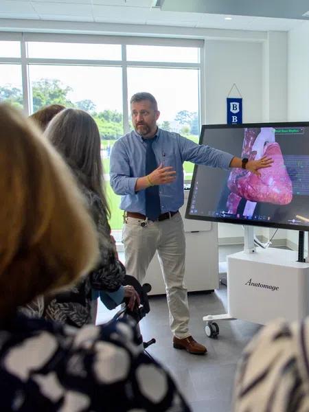 Person giving a medical presentation on a digital lung model to an audience in a bright classroom.