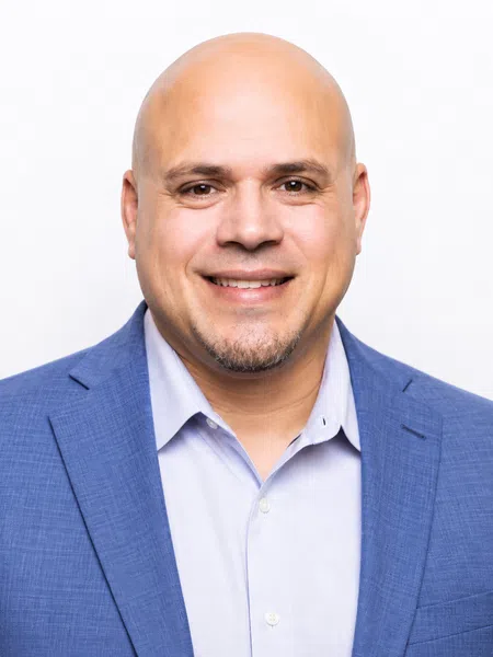 Smiling bald man in blue blazer and light blue shirt against a plain white background.