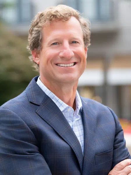 Smiling man in blue checkered suit with arms crossed outdoors in an urban setting