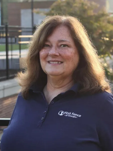 Smiling woman in a navy blue First Fence of Georgia polo shirt outdoors with a fence and greenery in background