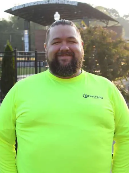 Smiling man with beard wearing neon yellow First Fence shirt in front of an outdoor amphitheater.
