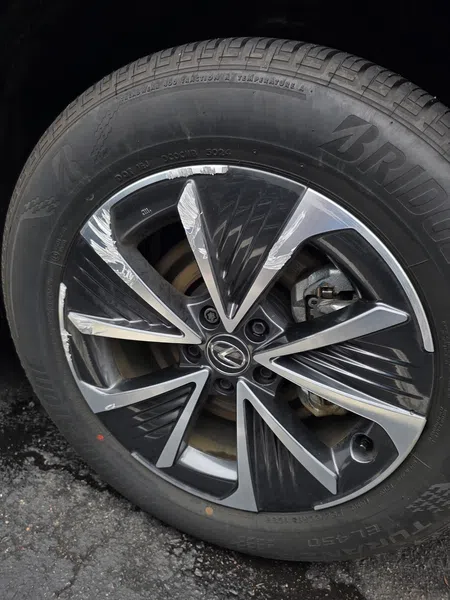 Close-up of a black and silver Lexus alloy wheel with Bridgestone tire on asphalt surface.