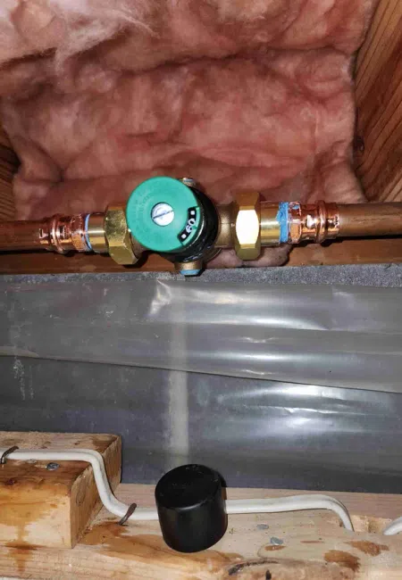 Copper pipe with green valve installed inside a wooden framed wall with pink insulation.