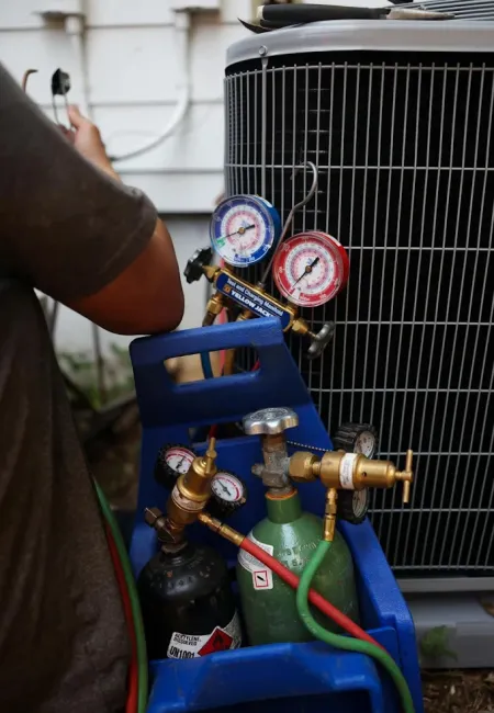 Close-up of HVAC technician using pressure gauges and gas tanks to service an air conditioning unit outdoors