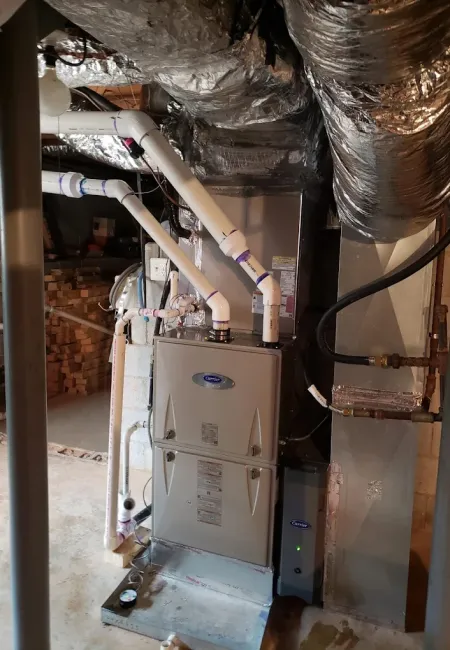 Furnace and duct system with insulated pipes in a residential basement with concrete floor and walls.
