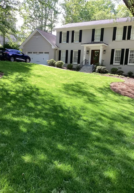 Two-story white house with black shutters, a well-kept lush green lawn, and a parked SUV near garage in daylight
