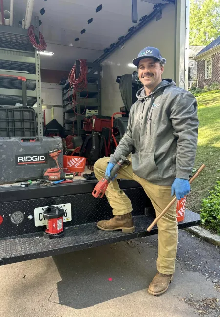 A technician stands next to a truck filled with tools and equipment, ready for plumbing work.