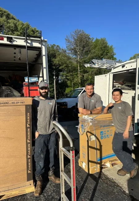 Three HVAC technicians standing by delivery trucks with Daikin air conditioning units outdoors on a sunny day.