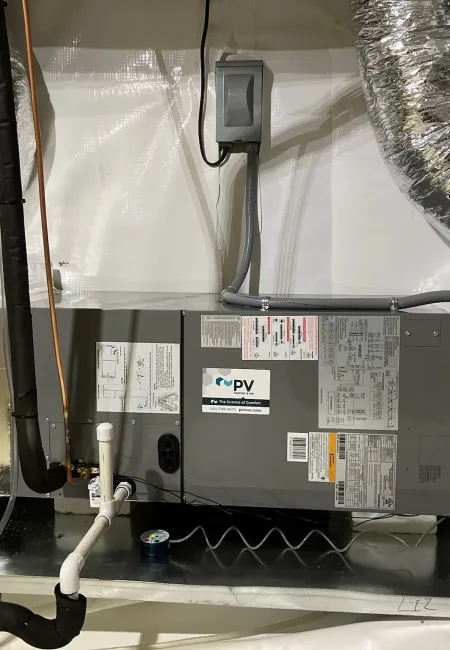 Indoor HVAC system with insulated ducts, gray unit, and white PVC pipes installed on metal surface in basement.