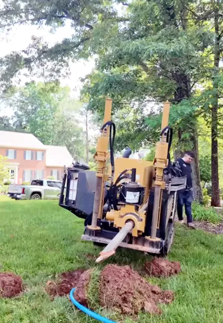 Horizontal directional drilling machine digging underground near residential house with worker and green trees