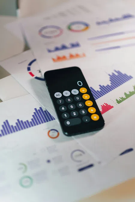 Smartphone calculator app on printed financial charts with colorful graphs and data visualizations.