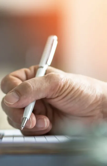Close-up of a hand writing on paper with a stethoscope and blood pressure monitor in the background