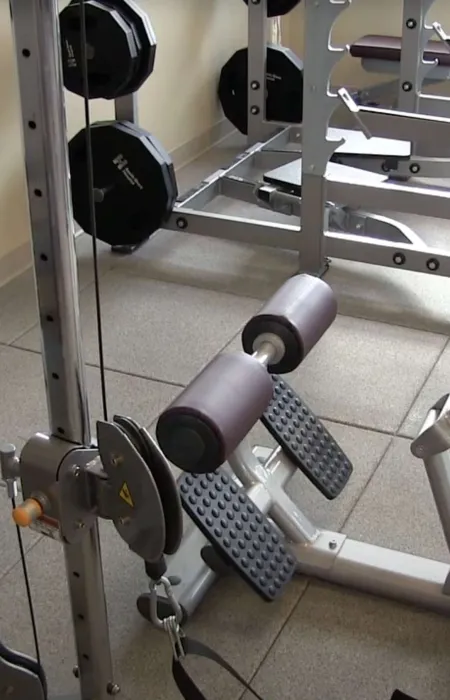 Gym fitness equipment including weight machine, leg curl machine, and dumbbells in a workout room.