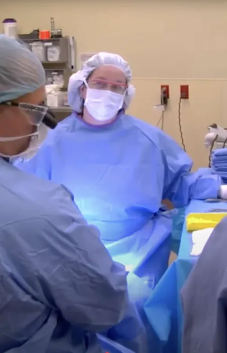 Medical team in surgical scrubs and masks performing an operation in a sterile hospital operating room.