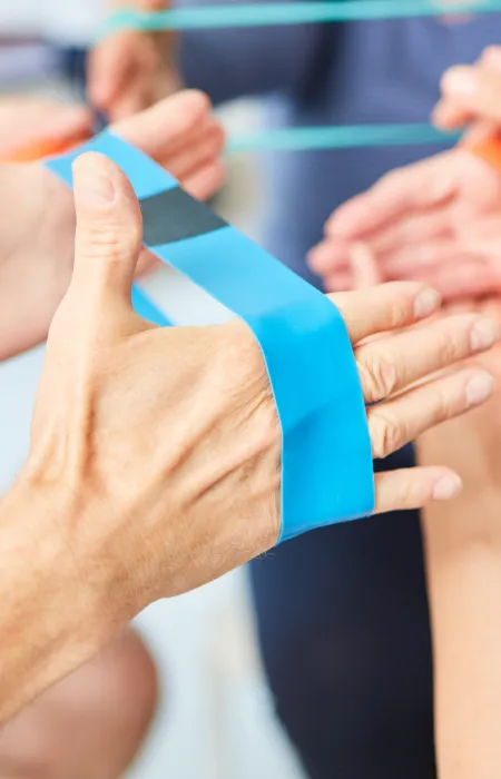 Close-up of hands using colorful resistance bands for group physical therapy or exercise session.