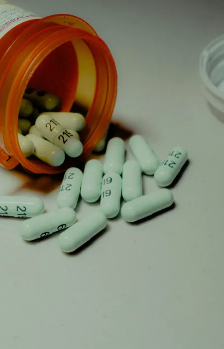Orange prescription bottle tipped over with white capsules spilling on a white surface.