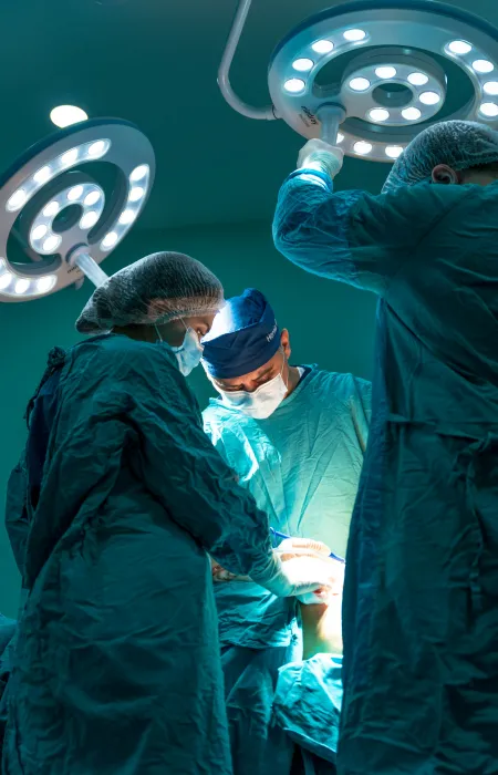 Surgeons in blue scrubs perform surgery under bright operating room lights in a sterile environment