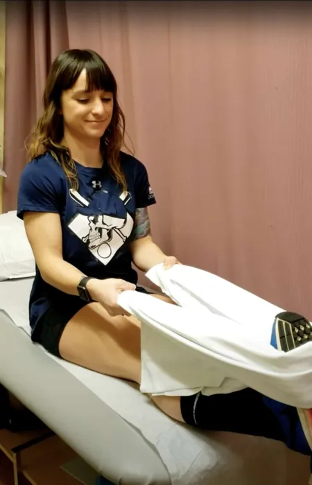 Female therapist assisting patient with leg exercise on medical table in clinic setting.