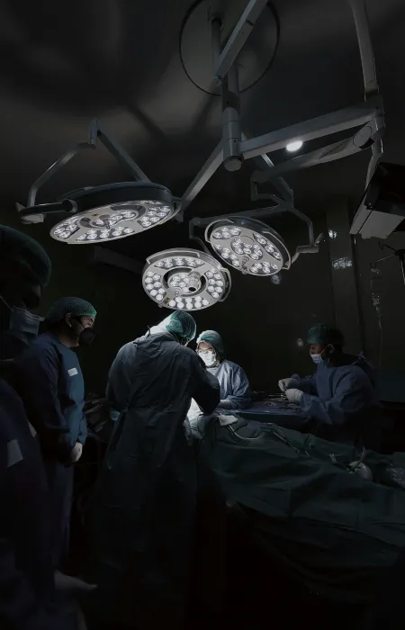 Surgeons in protective gear performing surgery under bright operating room lights in a dark environment.