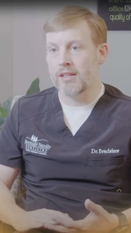 Male dentist Dr. Bradshaw in Heritage Family Dentistry uniform speaking during an interview in office.