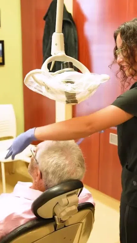 Dentist in gloves preparing dental light for elderly male patient reclining in dental chair
