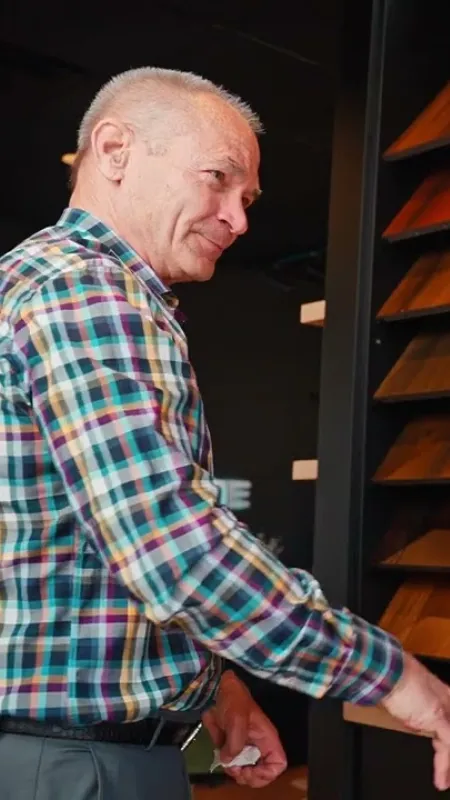 Two men discussing wood flooring samples displayed on a wall in a showroom with various wood finishes.