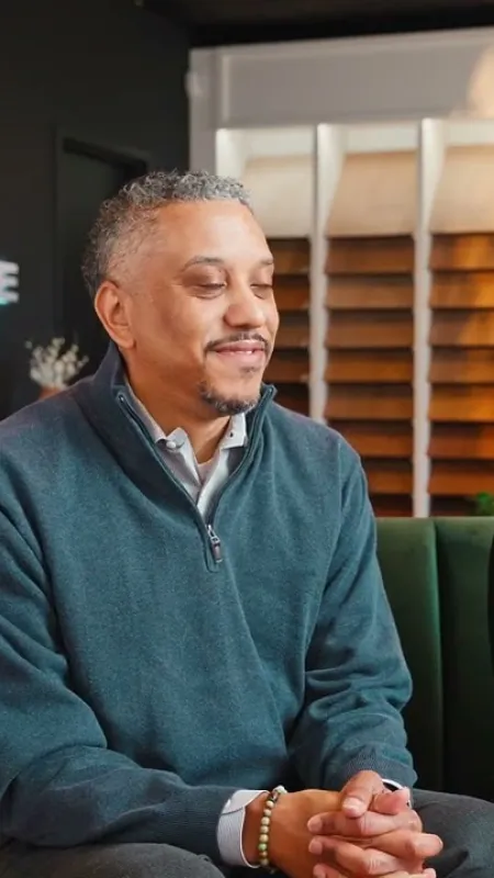 Two people seated on a green couch inside a peach state hardwood showroom with flooring samples in background.
